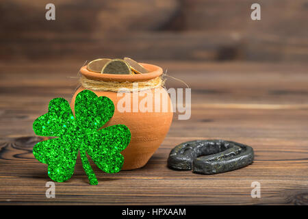 Il giorno di San Patrizio decorazione con pentola di monete d'oro, a ferro di cavallo e luce shamrock su vintage sfondo di legno, close up Foto Stock