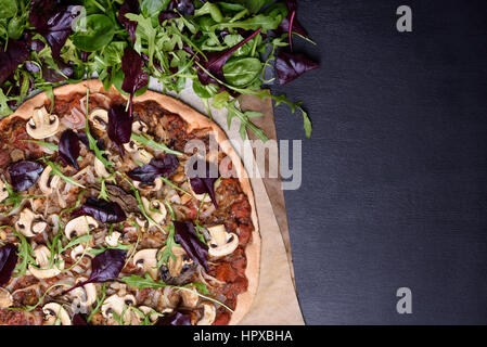 Pizza italiana e insalata primavera mescolare con la rucola (rucola) sul legno scuro dello sfondo. Vista aerea, copia dello spazio. Foto Stock