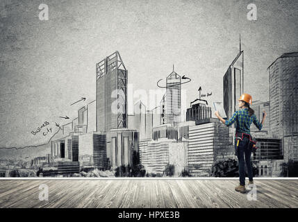 Vista posteriore di ingegnere di donna con la cartella e schizzi di progetto di costruzione sulla parete Foto Stock