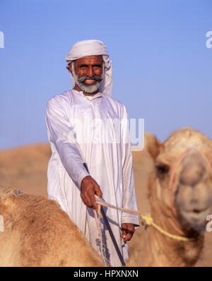 Sorridente camel driver con cammello nel deserto di Dubai, Dubai, Emirati Arabi Uniti Foto Stock