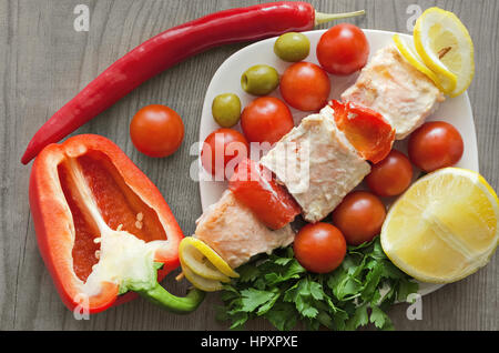 Spiedini di salmone su una piastra con verdure e verdi. Sfondo di legno. Foto Stock