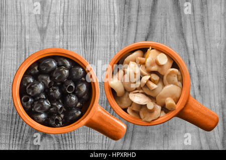 Marinata di funghi e olive in una coppa in ceramica, su un livello di grigio sullo sfondo di legno. La vista dall'alto. Foto Stock