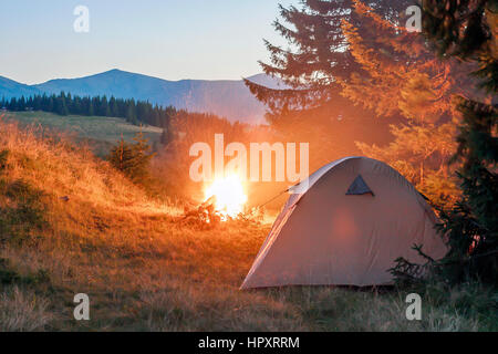 Tenda per gli escursionisti in montagna in serata con un falò con scintille vicino Foto Stock