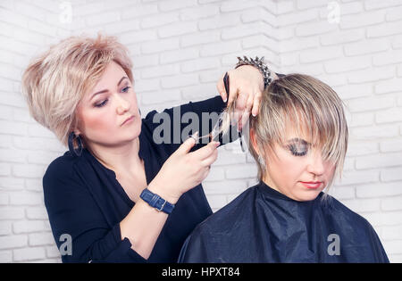 Donne's Haircut. Parrucchiere e salone di bellezza. Ritratto di professional parrucchiere donna di mezza età rendendo elegante taglio di capelli. Processo di taglio di capelli wit Foto Stock