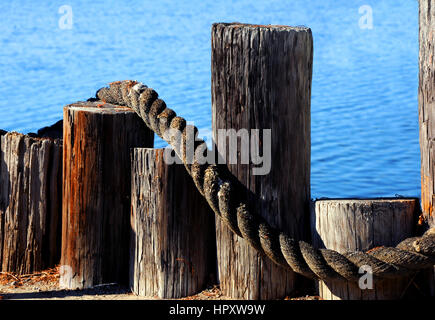 Palificazioni di dock, in altezze variabili, formare barriera tra la terra e il mare. Spessore corda intrecciata stabilisce attraverso staccionata in legno. Foto Stock