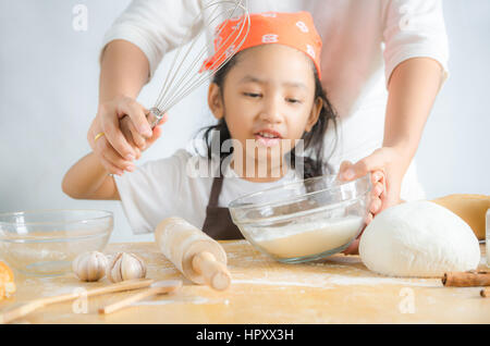 Immagine ravvicinata Asian bambina tenendo in acciaio inox frusta e panificio impasto di farina nella ciotola di vetro e madre mani, concentrarsi sulle mani profondità di f Foto Stock