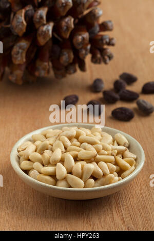 Ciotola con pinoli con pinoli, pigna in background Foto Stock