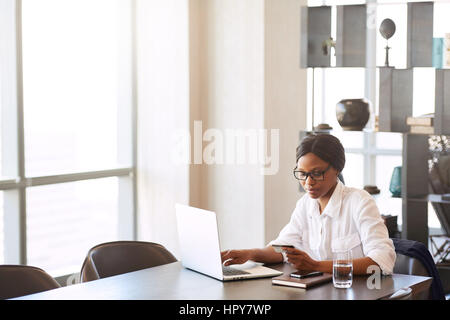 Ampia immagine della giovane donna nera occupate a tenere la sua carta di credito nella sua mano come essa rende i bonifici bancari per lo shopping on line ha fatto su internet f Foto Stock