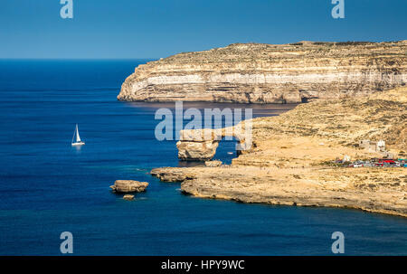 A Gozo, Malta - Azure Window e Dwejra Bay su una bella giornata d'estate con la barca a vela e cielo blu chiaro Foto Stock