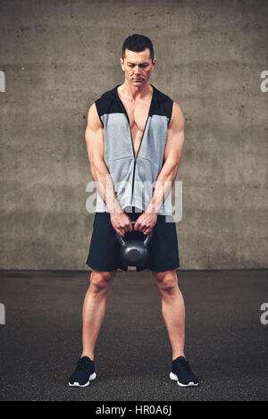 Giovane uomo forte in azienda di abbigliamento sportswear kettlebell pesanti su sullo sfondo di un muro di cemento. Foto Stock