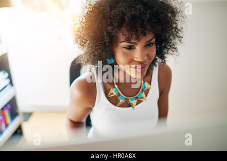 Attraente giovane donna afro-americana lavora al computer in ufficio. Copyspace Foto Stock