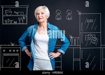 Assolutamente immacolato. Felice il piacere di età donna in piedi in cucina e sorridente pur essendo orgogliosi della pulizia in camera Foto Stock