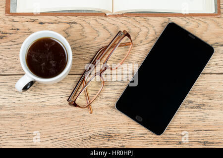 Ancora la vita di uno smartphone, occhiali, una tazza di caffè e un libro sul vecchio tavolo in legno Foto Stock