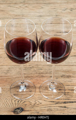 Due bicchieri di vetro con un bicchiere di vino rosso in piedi accanto ad un vecchio tavolo in legno Foto Stock