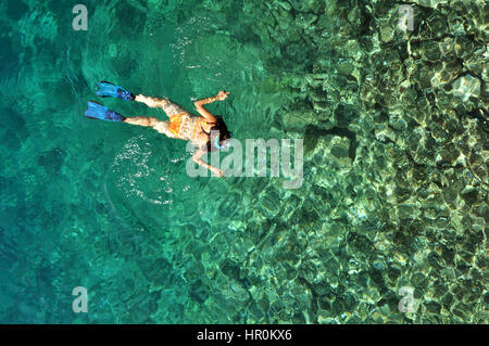 Giovane donna in costume da bagno lo snorkeling in chiaro poco profondo mare tropicale oltre le barriere coralline Foto Stock