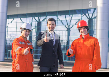 Sorridente manager e i costruttori gesticolando pollice in alto. All'aperto orizzontale shot. Foto Stock