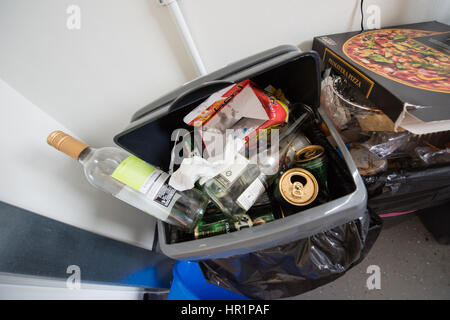 Traboccante di sporco in plastica da cucina swing scomparti pieno di spazzatura, scatole per pizza, bottiglie di vino e lattine di birra in una sala studenti del residence cucina comune Foto Stock