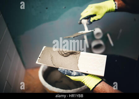 Industrial close up dettaglio del lavoratore l'aggiunta di collante cementizio su piccole piastrelle in ceramica Foto Stock