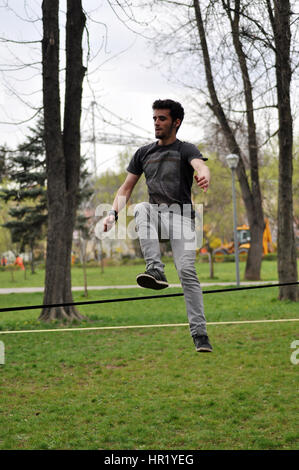 A Cluj Napoca, Romania - Aprile 1, 2016: un ragazzo che fa slackline trucchi nel Central park durante il grande giorno amaca Foto Stock