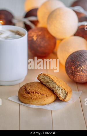 Biscotti dolci su legno sfondo naturale. Vicino il cookie è bianco cup con caffè e white marshmallows. In background incandescenza fari tondi. Foto Stock