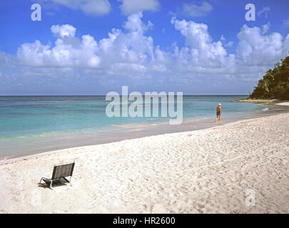 Solo l'uomo camminare chiaro calme acque turchesi del Mare dei Caraibi foreshore bianco costa sabbiosa Long Bay Beach Antigua West Indies Isole Sottovento dei Caraibi Foto Stock