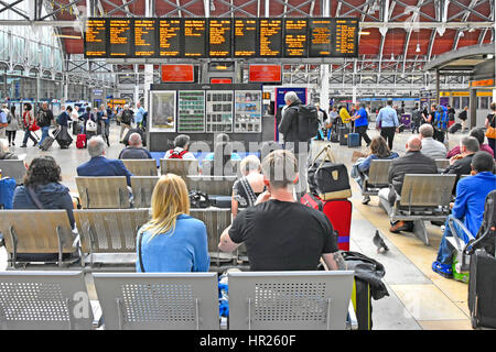 Stazione ferroviaria di Paddington concourse treno passeggeri seduti da elettronici schede di partenza in attesa di treni Orari Destinazioni & dettagli sulla piattaforma Foto Stock