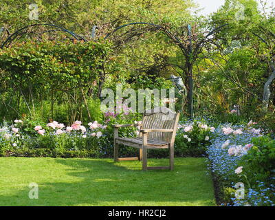 Panchina da giardino in Chenies Manor Garden nel maggio mostra il awn, arcata e di rosa pastello con tulipani underplanting di blu Dimenticare me not Foto Stock