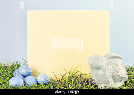 Segno vuoto con spazio copia tinti con le uova di Pasqua e un generico bunny in erba contro uno sfondo blu. Foto Stock