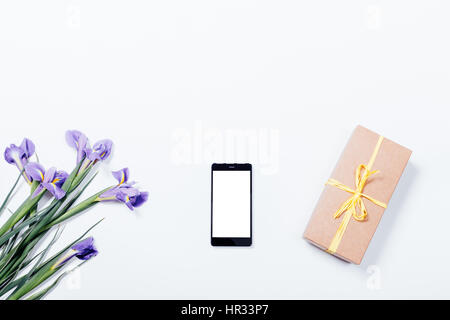 Bouquet di iridi viola, telefono cellulare e confezione regalo su sfondo bianco, vista dall'alto Foto Stock