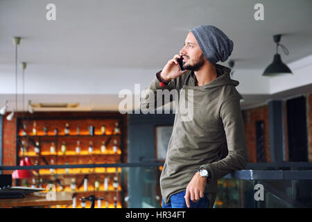 Giovane bello hipster uomo utilizza lo smartphone in cafe Foto Stock