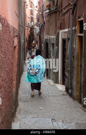 Marrakech, Marocco. Donna bambino portando sulla schiena in una strada stretta della Medina. Foto Stock