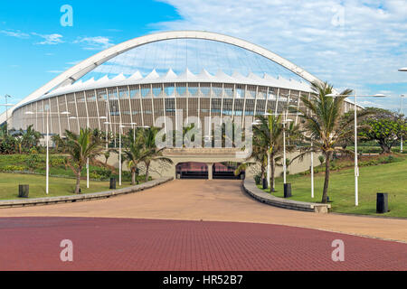 DURBAN, Sud Africa - 24 febbraio 2017: la mattina presto, pavimentato promenade, verde prato e alberi di palma contro Mosè Mabhida Stadium e il clou di colore blu Foto Stock