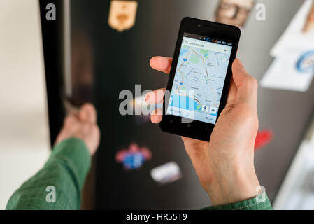 Close-up di persona mani tenendo lo smartphone che mostra una mappa della città su schermo e di ricerca online per i luoghi dove mangiare in questa mappa. Frigorifero con magneti o Foto Stock