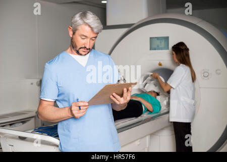 Medico di sesso maschile negli appunti di lettura con il collega di sesso femminile preparazione paziente per MRI scan in ospedale Foto Stock