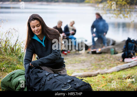 Giovane donna disimballaggio zaino con amici in background in campeggio Foto Stock