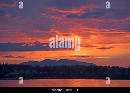 Un profondo ricco tramonto sul mare verso Parksville cittadina e la Arrowsmith montagne dietro. Foto Stock