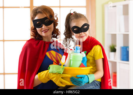 Carino bambino ragazza e sua madre per effettuare la pulizia della casa. Bambina e la mamma sono vestiti in costumi del superman. Foto Stock