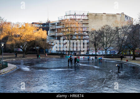 Berlino, Mitte, Volkspark am Weinbergsweg. La gente a piedi e giocare su un laghetto congelato in un parco pubblico in inverno Foto Stock