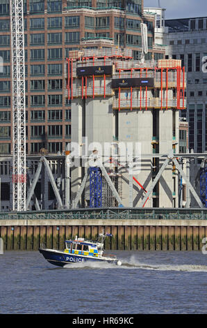 Una polizia velocità di lancio lungo il fiume Tamigi a Londra, Regno Unito, passando un sito in costruzione a Canary Wharf. Foto Stock