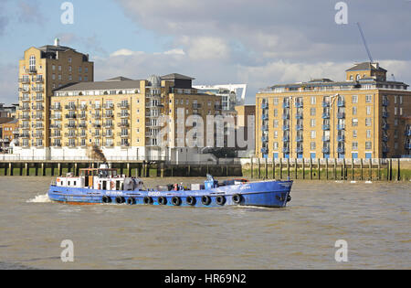 Un piccolo diesel vele di navi cisterna a valle sul fiume Tamigi a Londra, passando moderni loft appartamenti in stile Wapping Foto Stock