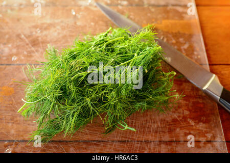 Rametti di verde e fresco con aneto gocce di acqua su un tavolo di legno. Grande Coltello metallico su uno sfondo naturale. Messa a fuoco selettiva. Foto Stock