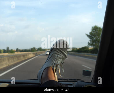 Furgoni scarpe di tela sul cruscotto di un'auto accelerando su una autostrada Foto Stock