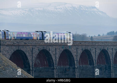 Un Arriva Ferrovia Nord diesel passeggeri dei treni attraverso il viadotto Ribblehead sul grigio di una giornata invernale con snow-capped Pen-y-Ghent al di là. Foto Stock