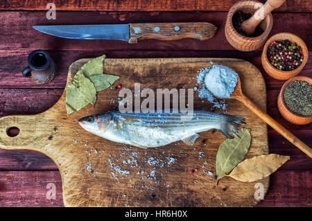 Pesce fresco odore per la cottura su una scheda di cucina, nei pressi di spezie in vasi di legno Foto Stock