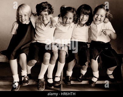 Retrò Educazione SCUOLA JUNIOR FELICE NATURALE GRUPPO bambino 5-7 anni 3 ragazze e 1 Ragazzo che sorride seduto sul banco di scuola, realizzata per Kodak Arte di 35mm libro. Immagine B&W Kodak Tri-X film studio degli alunni della scuola primaria insieme seduta sul banco in luce naturale, godendo di essere insieme e avente una scuola informale prendere foto..Ian Shaw fotografo Kodak Foto Stock