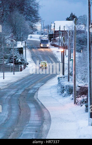 In inverno le condizioni di guida a causa della neve sulle strade nel villaggio di Rhosesmor in Flintshire, il Galles del Nord come conducenti di commutare in mattinata il traffico attraverso la strada principale che attraversa il villaggio Foto Stock
