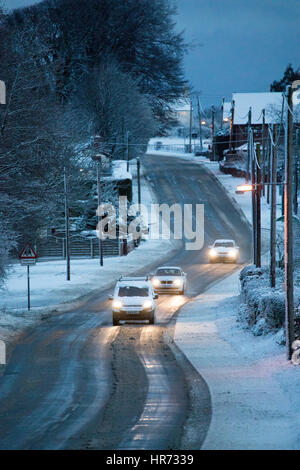 In inverno le condizioni di guida a causa della neve sulle strade nel villaggio di Rhosesmor in Flintshire, il Galles del Nord come conducenti di commutare in mattinata il traffico attraverso la strada principale che attraversa il villaggio Foto Stock