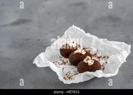 Dolci a base di cioccolato su un bianco carta trasparente su sfondo grigio. Torte decorate con gelatina rossa e delicata crema bianca. Foto Stock