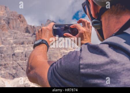 Scattare foto utilizzando dispositivo Smartphone. Caucasian Biker in bici casco di scattare una foto della montagna panoramica posto. Foto Stock