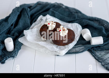 Dolci a base di cioccolato su carta trasparente su uno sfondo bianco. White marshmallows. Torte decorate con gelatina rossa e delicata crema bianca. Blue Foto Stock